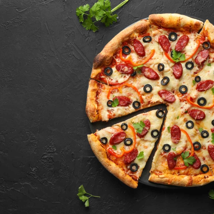 Tasty pizza with dry smoked sausages, olives, pepper and parsley on black table, top view. Space for text Tasty pizza with dry smoked sausages, olives, pepper and parsley on black table, top view. Space for text
